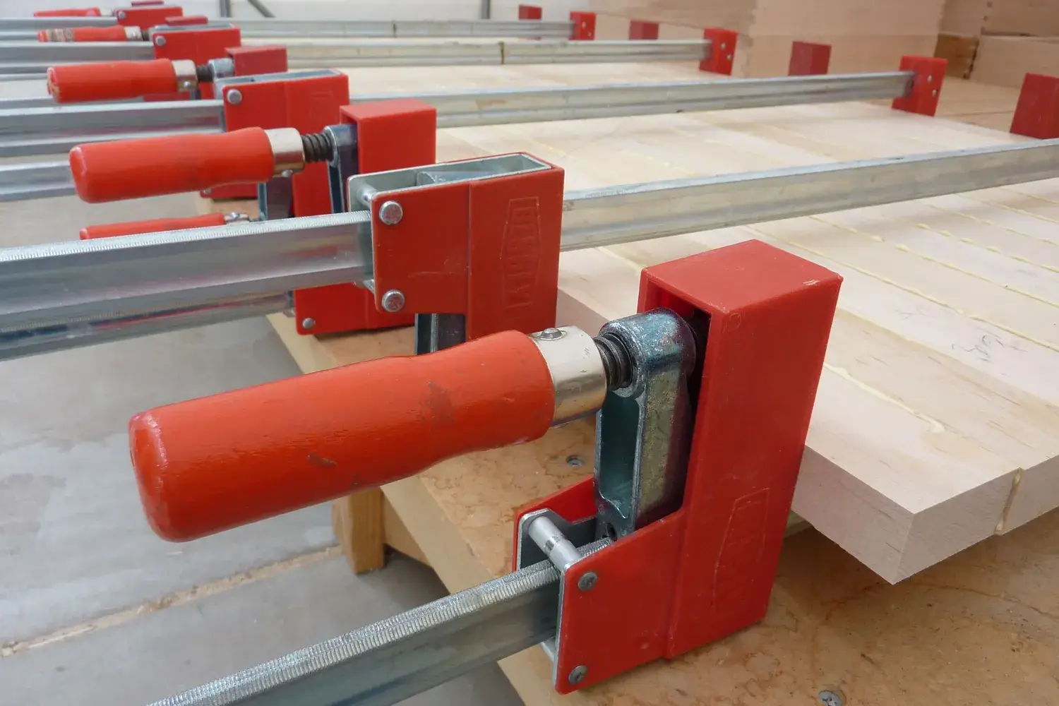 A row of red bar clamps holding boards together during a panel glue-up